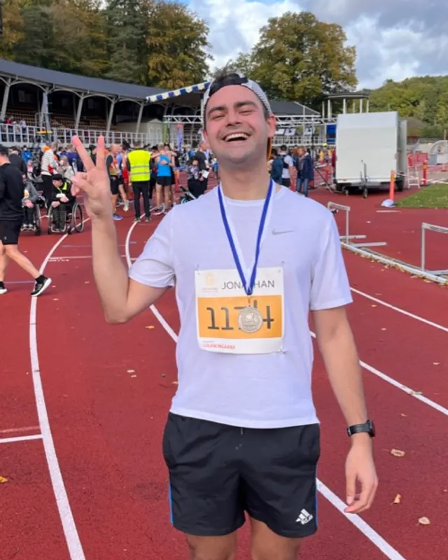 Jonathan, grinning and holding up a peace sign on a running track after a race